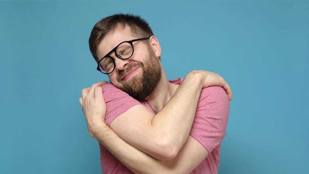 Mann umarmt sich selbst – nährende Selbstberührung als Zeichen für mehr Selbstliebe