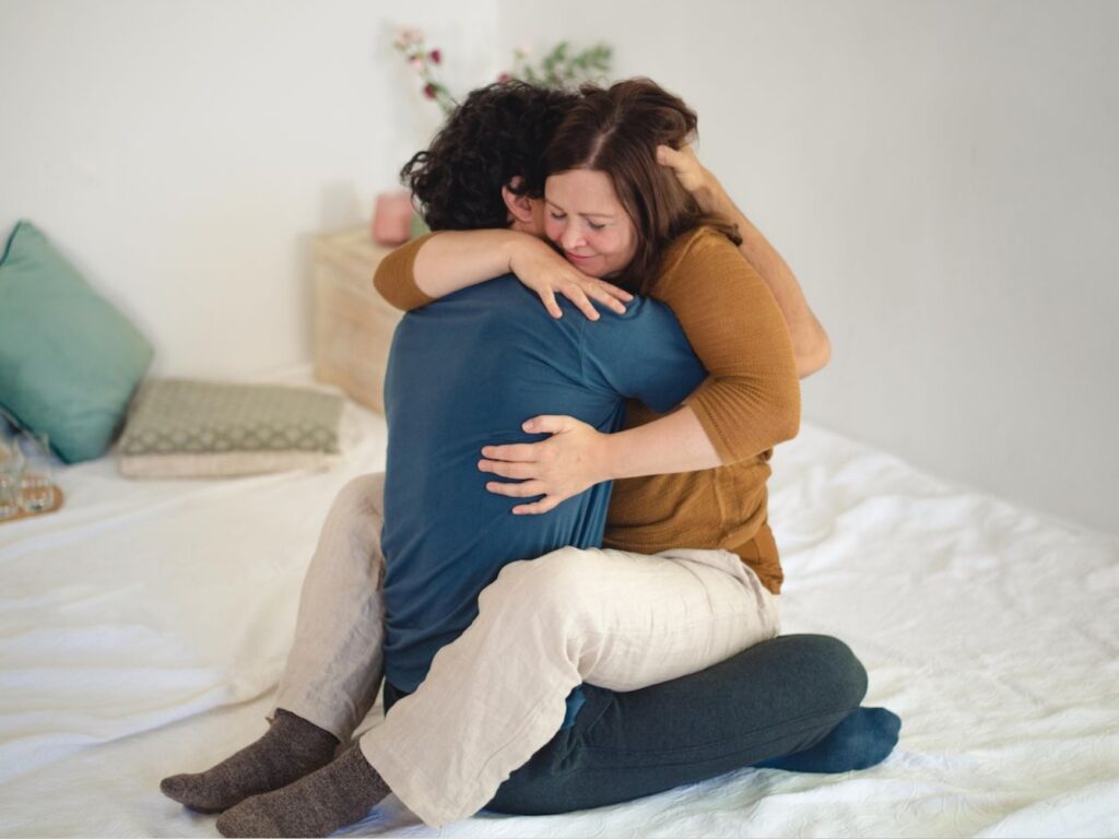 Zwei Menschen sitzen in einer innigen Umarmung, die Verbundenheit, Vertrauen und tiefe Präsenz ausdrückt.