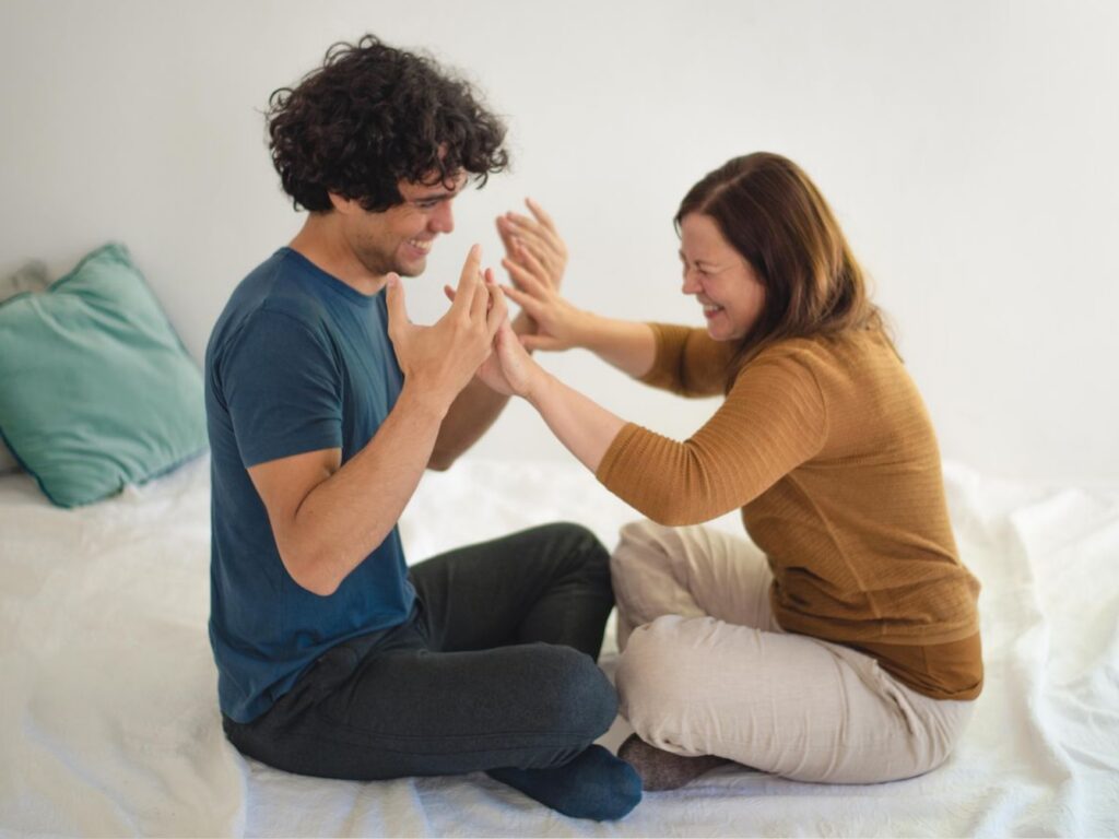 Zwei Menschen erleben eine berührende Übung, halten sich an den Händen und lachen in einem sicheren, achtsamen Rahmen.