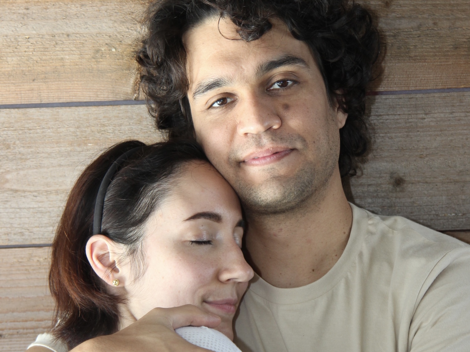 Kuscheltherapeut lächelt in die Kamera, eine Klientin liegt entspannt in seinen Armen – ein Bild für Vertrauen, Geborgenheit und achtsame Berührung.